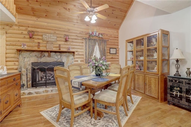 dining space with a stone fireplace, log walls, ceiling fan, light hardwood / wood-style floors, and wooden ceiling