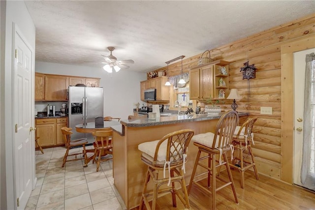 kitchen with a kitchen bar, hanging light fixtures, ceiling fan, kitchen peninsula, and stainless steel appliances