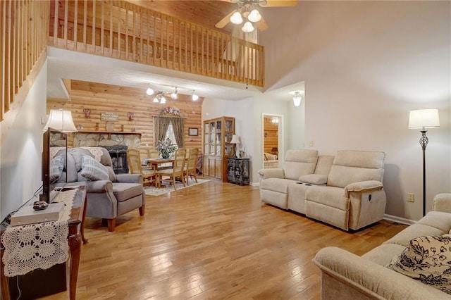 living room with a stone fireplace, a towering ceiling, log walls, ceiling fan, and light hardwood / wood-style floors