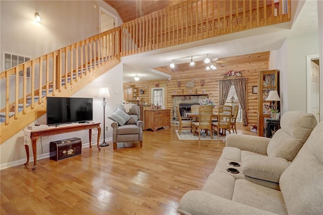 living room featuring ceiling fan, a high ceiling, a fireplace, wood-type flooring, and log walls