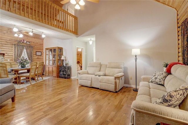 living room featuring ceiling fan, rustic walls, light hardwood / wood-style floors, and a high ceiling