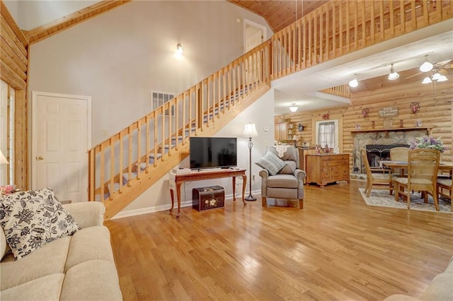 living room with a fireplace, rustic walls, high vaulted ceiling, and light hardwood / wood-style flooring