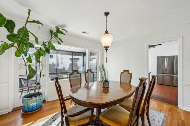 dining area featuring light wood-style floors, visible vents, and ornamental molding