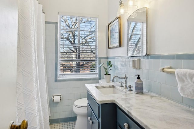 bathroom featuring a wainscoted wall, tile walls, toilet, and vanity