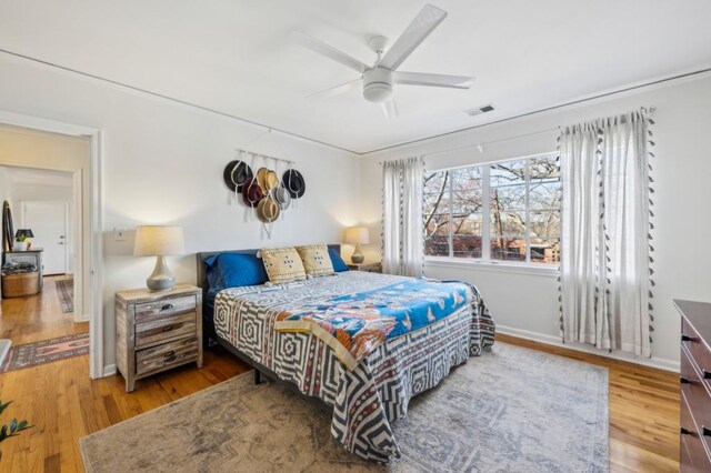 bedroom featuring a ceiling fan, wood finished floors, visible vents, and baseboards