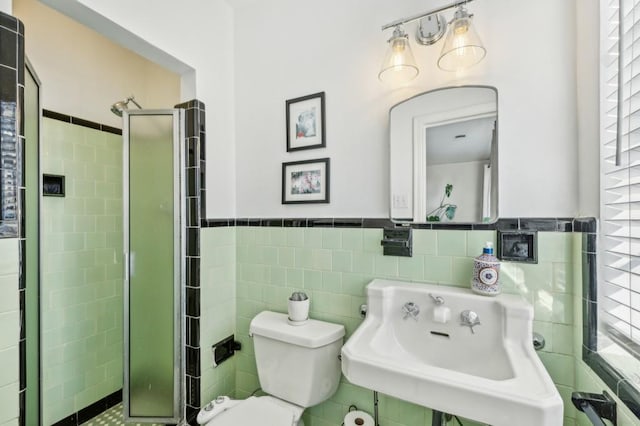 bathroom with toilet, a wainscoted wall, a sink, a shower stall, and tile walls