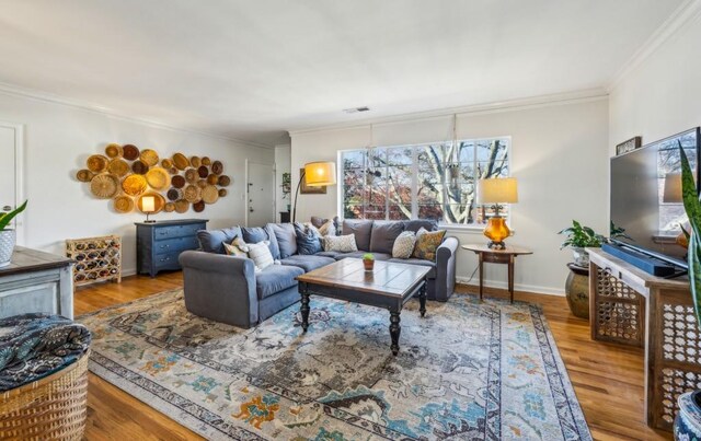 living area with baseboards, wood finished floors, visible vents, and crown molding