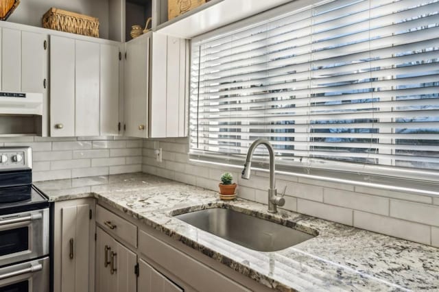 kitchen featuring white cabinets, light stone counters, under cabinet range hood, double oven range, and a sink