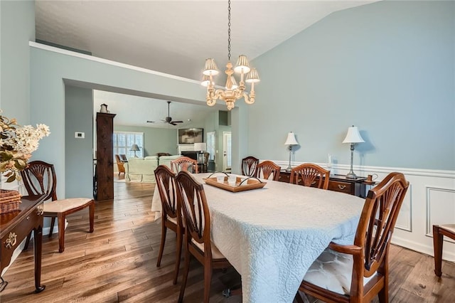 dining area with ceiling fan with notable chandelier, wood finished floors, wainscoting, and vaulted ceiling