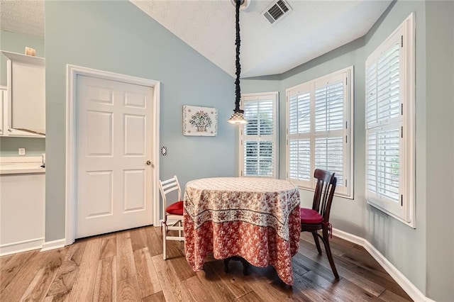 dining area with light wood-type flooring, visible vents, a textured ceiling, baseboards, and vaulted ceiling