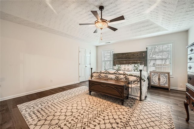 bedroom featuring a ceiling fan, dark wood-style floors, baseboards, a tray ceiling, and a textured ceiling