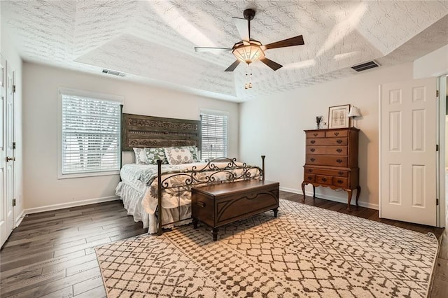 bedroom featuring visible vents, baseboards, a tray ceiling, wood finished floors, and a textured ceiling