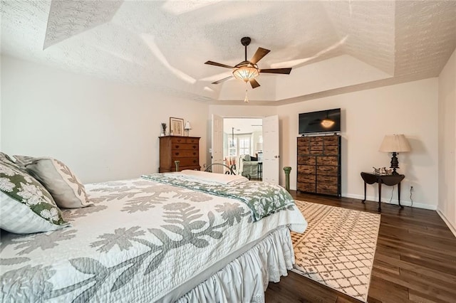 bedroom featuring baseboards, wood finished floors, a textured ceiling, a raised ceiling, and a ceiling fan