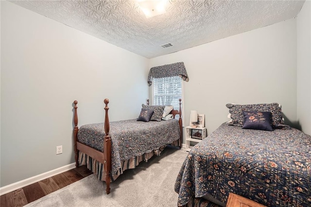 bedroom featuring wood finished floors, baseboards, visible vents, and a textured ceiling