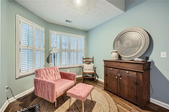 living area with a textured ceiling, wood finished floors, visible vents, and baseboards