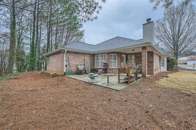 rear view of house with a patio, brick siding, a chimney, and a shingled roof