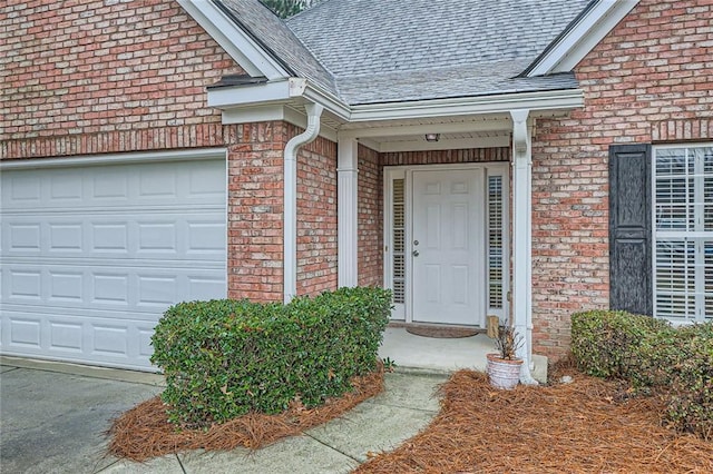 doorway to property featuring an attached garage, brick siding, and roof with shingles