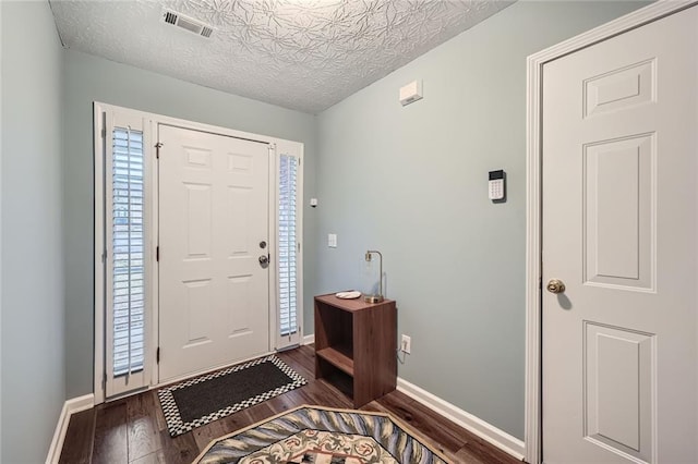 foyer featuring a textured ceiling, wood finished floors, visible vents, and baseboards