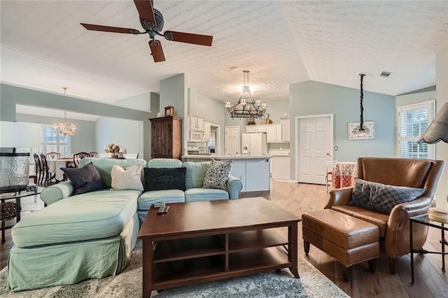 living area with visible vents, vaulted ceiling, ceiling fan with notable chandelier, light wood-style flooring, and a textured ceiling