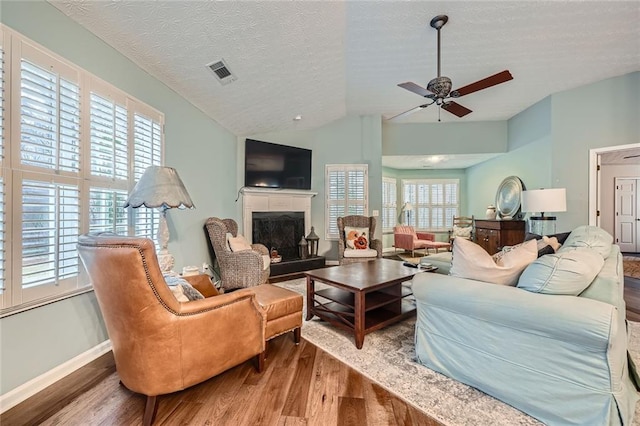 living area featuring visible vents, wood finished floors, a fireplace, ceiling fan, and vaulted ceiling