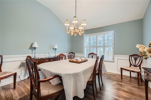 dining area with hardwood / wood-style floors, lofted ceiling, a notable chandelier, and a wainscoted wall