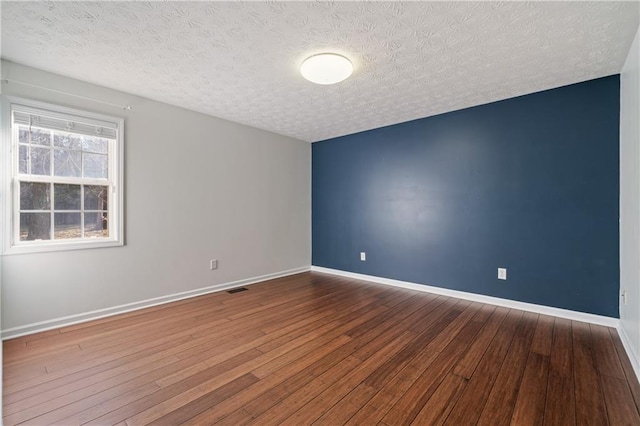 spare room featuring hardwood / wood-style flooring, visible vents, baseboards, and a textured ceiling