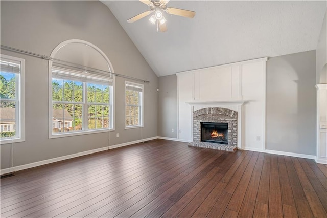 unfurnished living room with a wealth of natural light, a brick fireplace, dark wood-type flooring, and ceiling fan