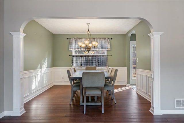 dining area with visible vents, arched walkways, an inviting chandelier, dark wood-style floors, and a decorative wall