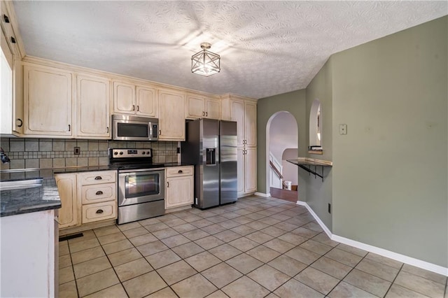 kitchen with a sink, backsplash, dark countertops, stainless steel appliances, and light tile patterned floors