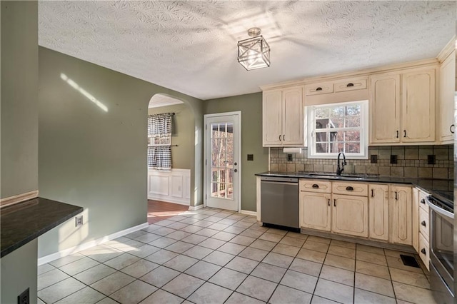 kitchen with arched walkways, a sink, appliances with stainless steel finishes, dark countertops, and tasteful backsplash