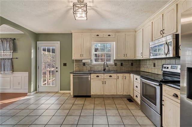 kitchen featuring decorative backsplash, dark countertops, light tile patterned flooring, and appliances with stainless steel finishes