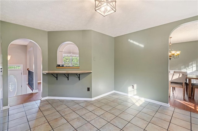 spare room featuring arched walkways, plenty of natural light, an inviting chandelier, and light tile patterned flooring