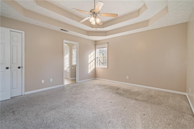 unfurnished bedroom featuring a tray ceiling, baseboards, visible vents, and carpet floors