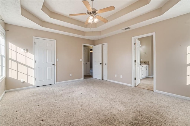 unfurnished bedroom with visible vents, baseboards, carpet floors, ensuite bathroom, and a raised ceiling