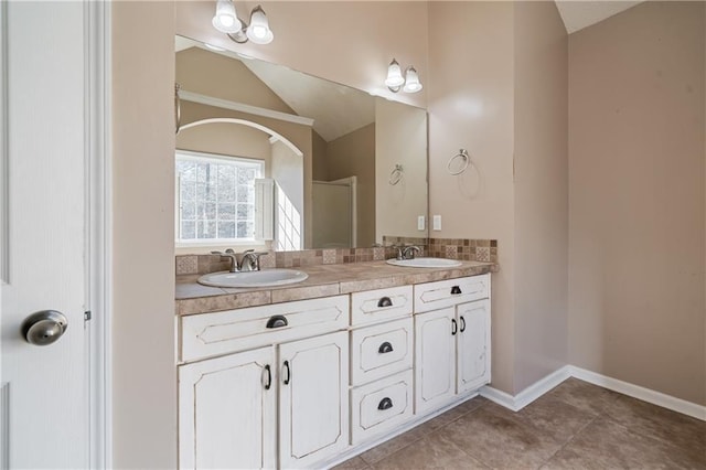 full bath with a sink, baseboards, lofted ceiling, and double vanity