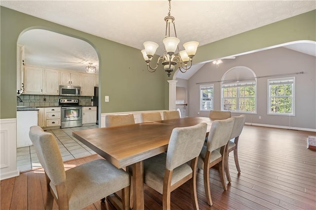 dining area featuring hardwood / wood-style floors, arched walkways, vaulted ceiling, a textured ceiling, and a notable chandelier