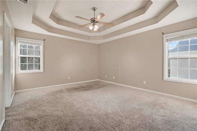 carpeted spare room with a tray ceiling, baseboards, and a ceiling fan