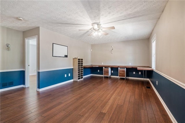 unfurnished room featuring a ceiling fan, baseboards, visible vents, hardwood / wood-style flooring, and built in desk