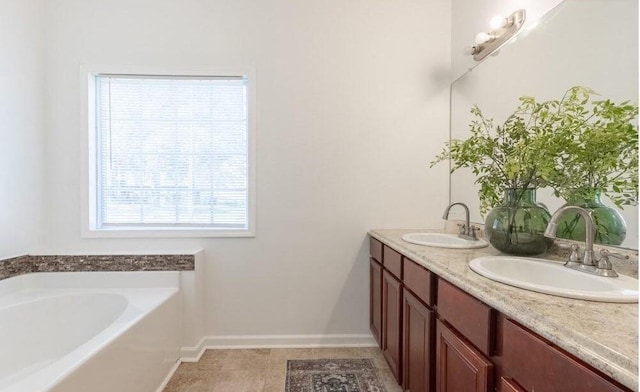 bathroom featuring a garden tub, double vanity, a sink, and baseboards
