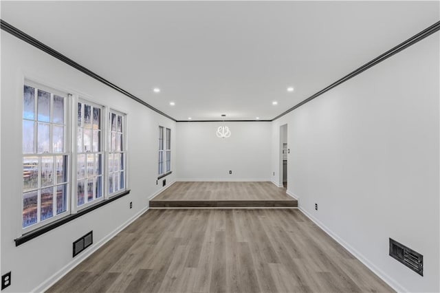 unfurnished room with a chandelier, light wood-type flooring, and crown molding