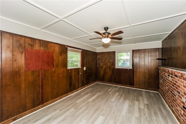 unfurnished room with a wealth of natural light, wood walls, ceiling fan, and light hardwood / wood-style flooring