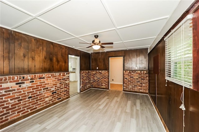 spare room featuring ceiling fan, brick wall, light hardwood / wood-style flooring, and wood walls