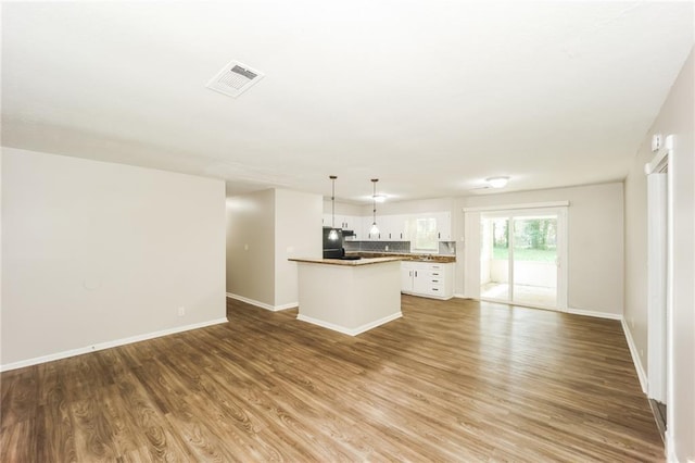 kitchen with white cabinetry, decorative light fixtures, black refrigerator, a kitchen island, and hardwood / wood-style floors