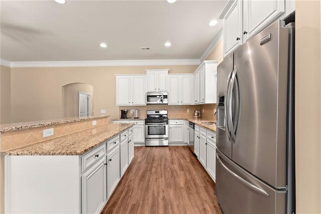 kitchen featuring light stone counters, appliances with stainless steel finishes, hardwood / wood-style floors, crown molding, and white cabinets