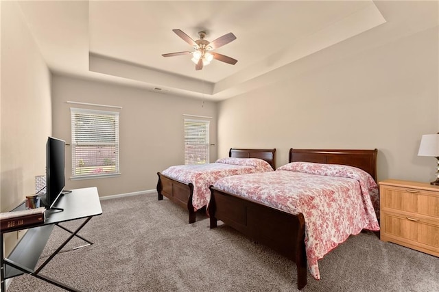 carpeted bedroom with ceiling fan and a raised ceiling