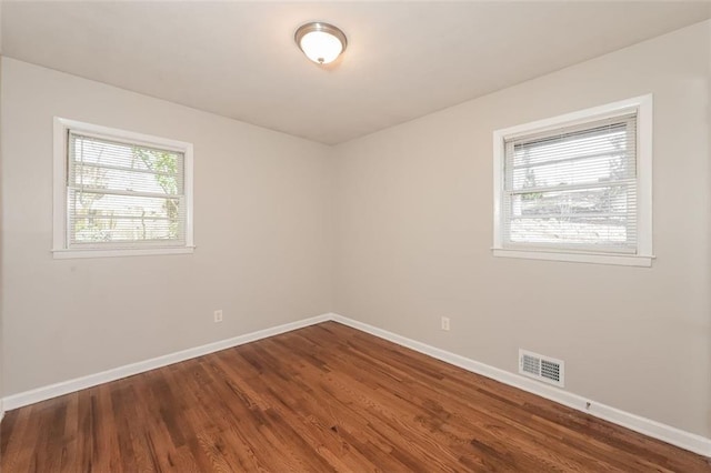 unfurnished room with visible vents, a healthy amount of sunlight, baseboards, and wood finished floors