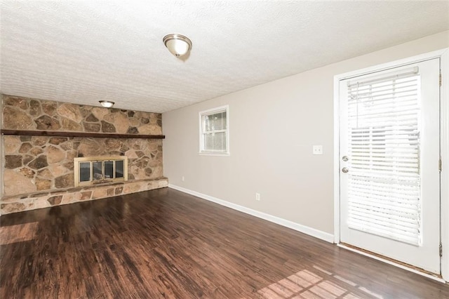 unfurnished living room with a stone fireplace, wood finished floors, baseboards, and a textured ceiling