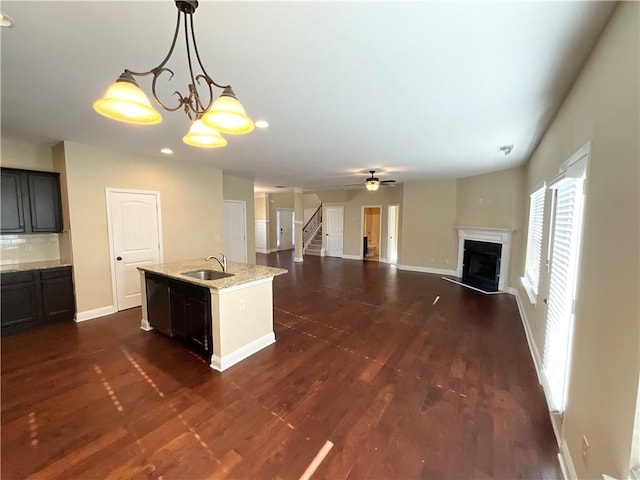 kitchen featuring a sink, a fireplace, baseboards, an island with sink, and dark wood-style floors