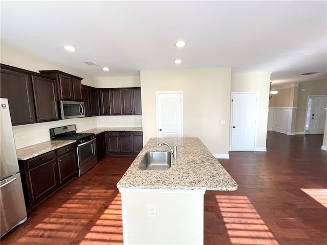 kitchen with stainless steel appliances, a sink, an island with sink, dark wood-style floors, and dark brown cabinets