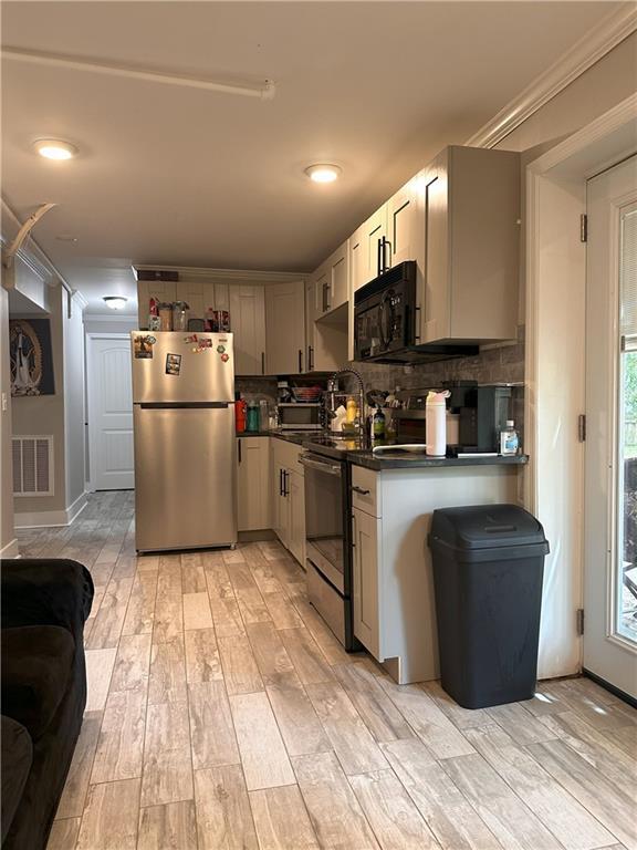1055 Worthington Hills Dr, Roswell, GA 30076 - kitchen featuring stainless steel appliances, dark countertops, light wood-style flooring, decorative backsplash, and ornamental molding